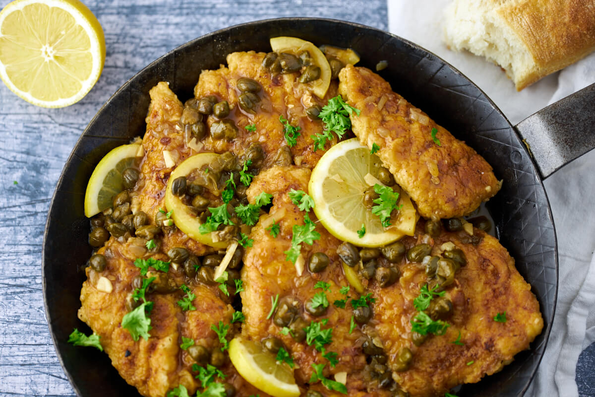 chicken piccata in pan with capers, lemon and parsley