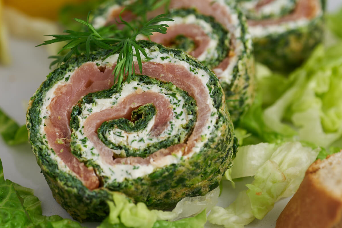 Spinach roulade with smoked salmon and cream cheese filling served with dill, lemon, lettuce and bread