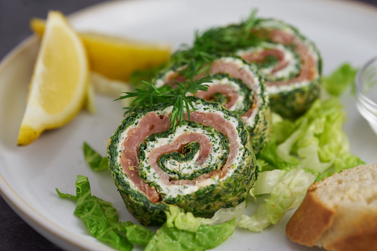 3 slices spinach roulade on plate with lettuce, lemon and flutes