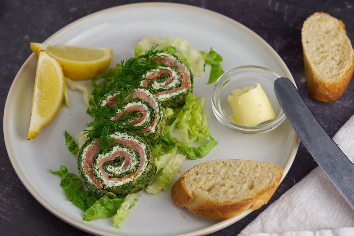 Plate of salmon roulade with spinach and cream cheese filling served with flutes butter and lemon