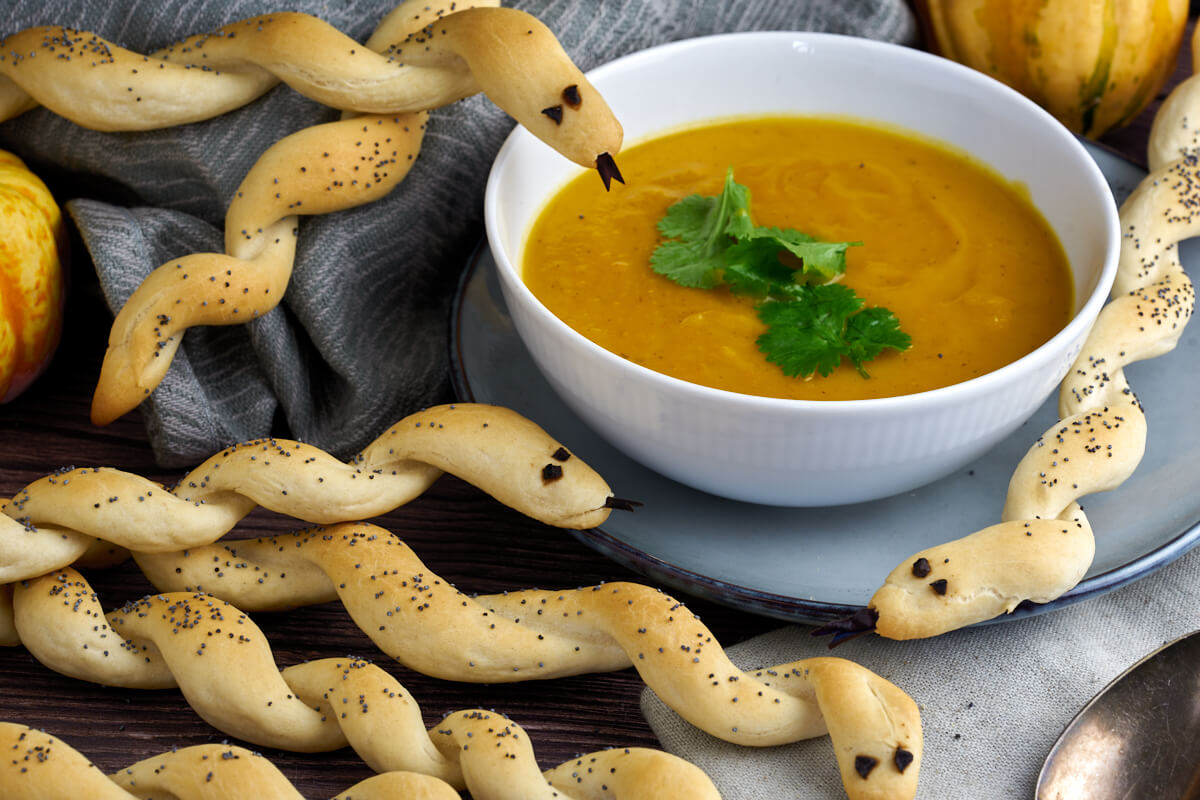 bowl of pumpkin soup and halloween breadsticks as snakes
