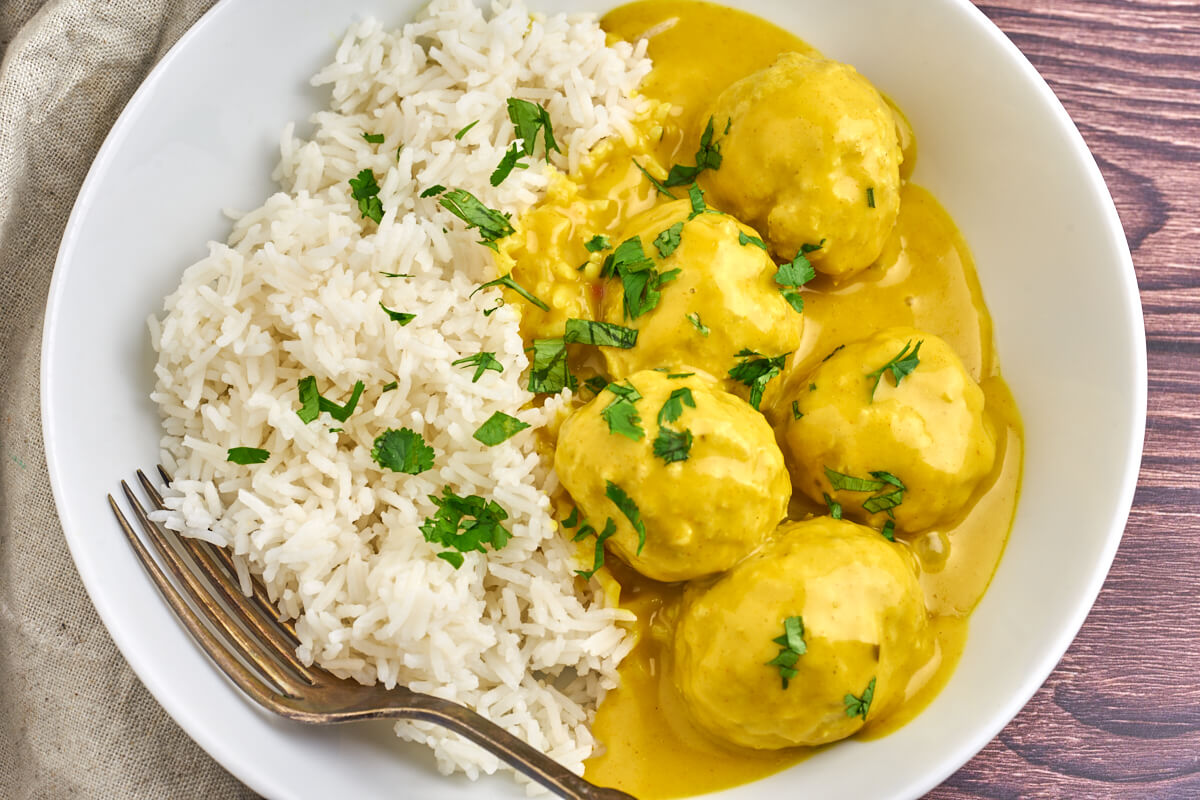danish meatballs in curry served with rice in a white plate