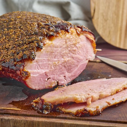baked glazed ham on chopping board with slices and a knife