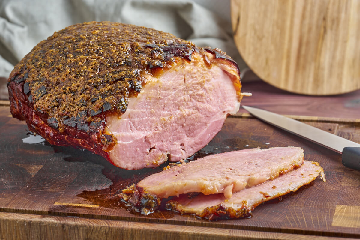 baked glazed ham on chopping board with slices and a knife