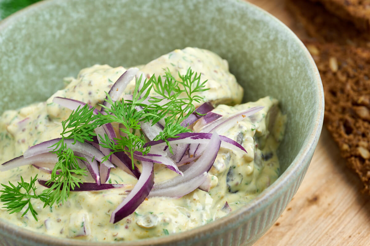 bowl with pickled herring in mustard saude with dill and red onion on top
