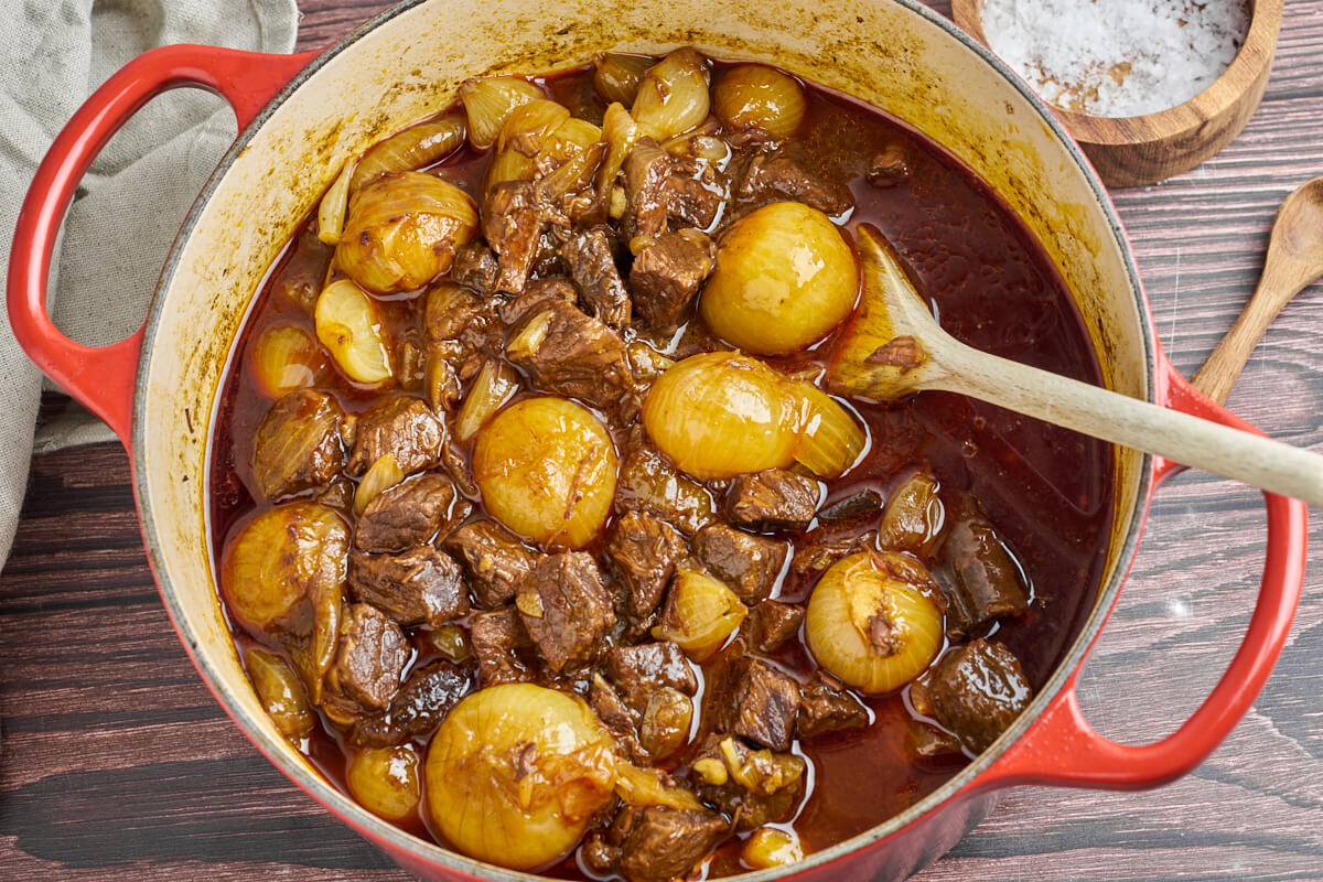 greek beef stifado with onions in a pot with a wooden spoon