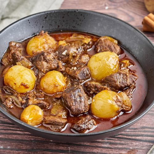 greek beef stifado in a plate with cinnamon and spoon