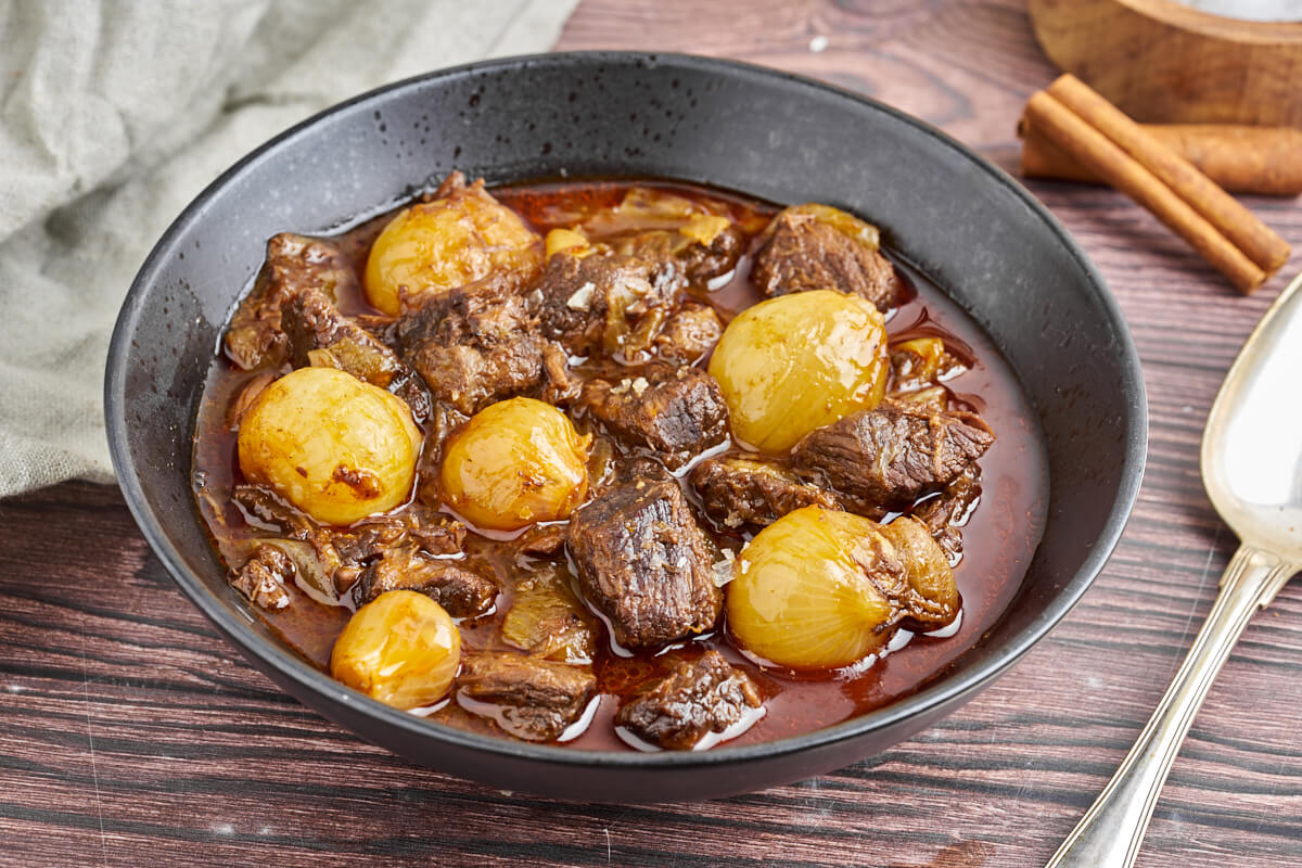 greek beef stifado in a plate with cinnamon and spoon