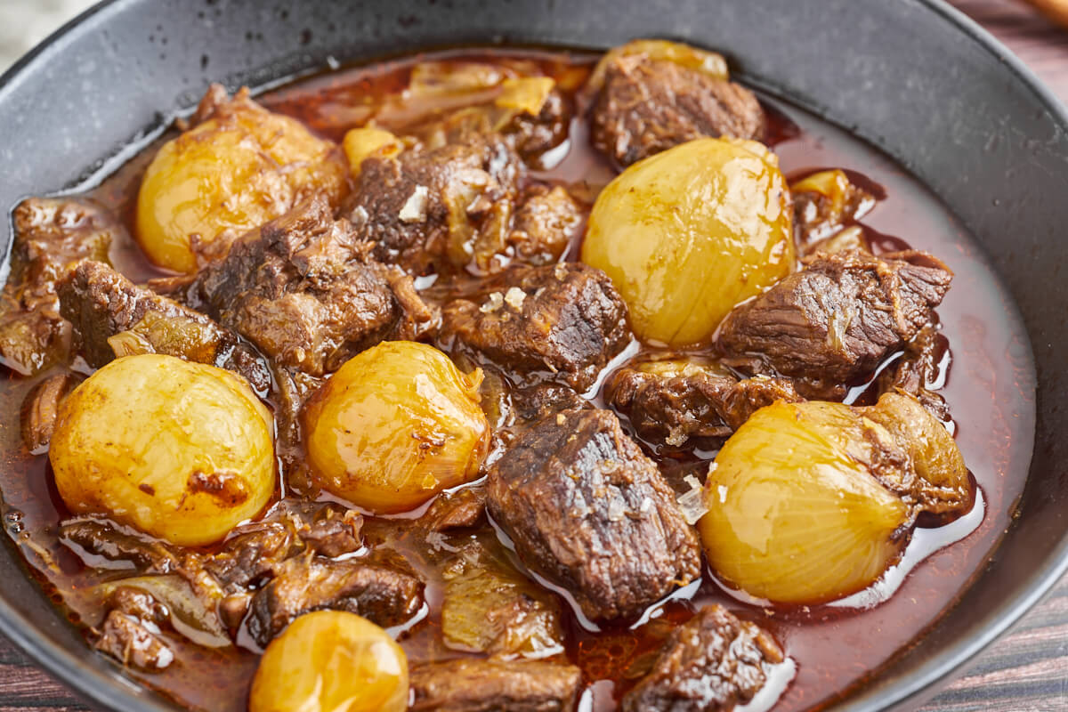 greek beef stifado with onions in black plate