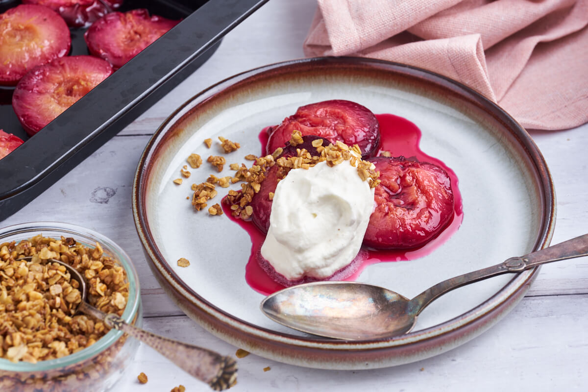 plate with baked plums with whipped cream and crumble and a small bowl with crumble and more plums in the background