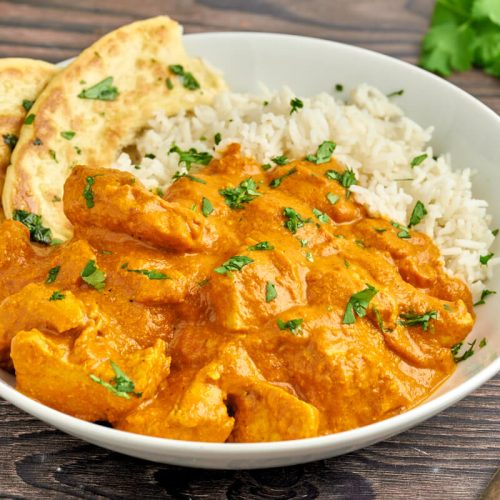 indian butter chicken with rice and naan bread on a plate with fork a cilantro