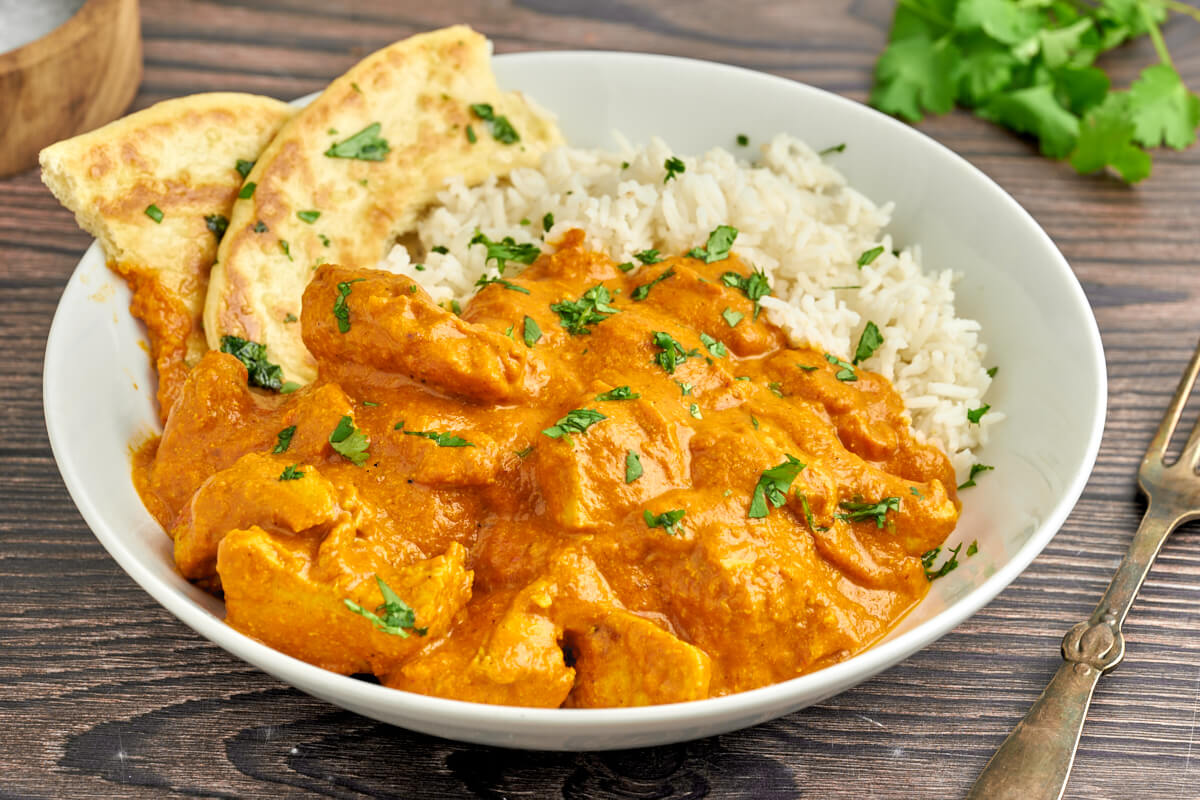 indian butter chicken with rice and naan bread on a plate with fork a cilantro