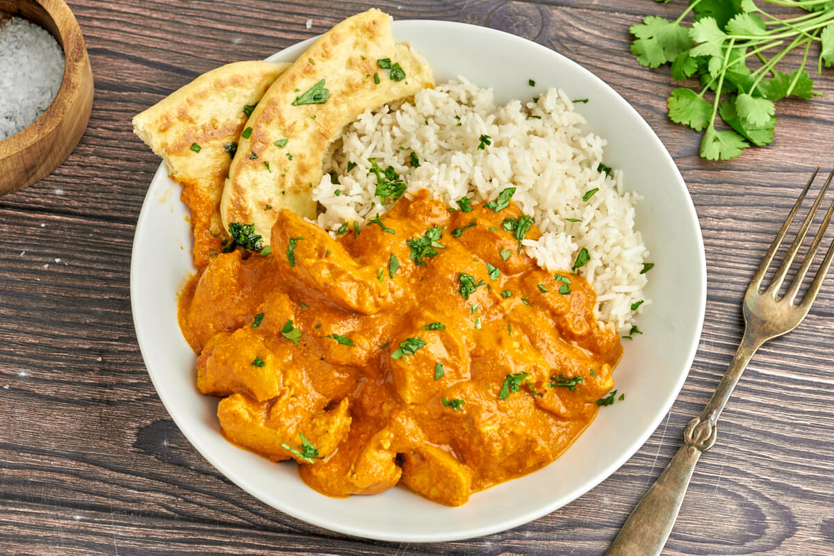 dish with indian butter chicken with rice and naan bread and topped with cilantro