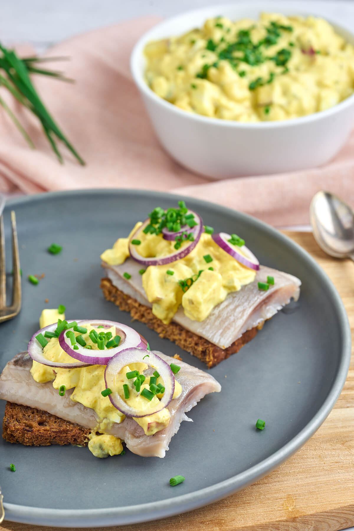 plate with two pieces of rye bread with marinated herring and danish curry salad with onion and chives