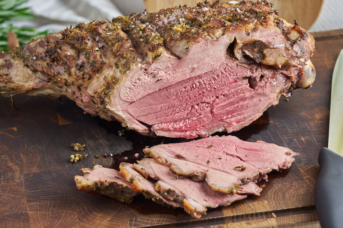 pink slow-roasted leg of lamb cut out on wooden chopping board