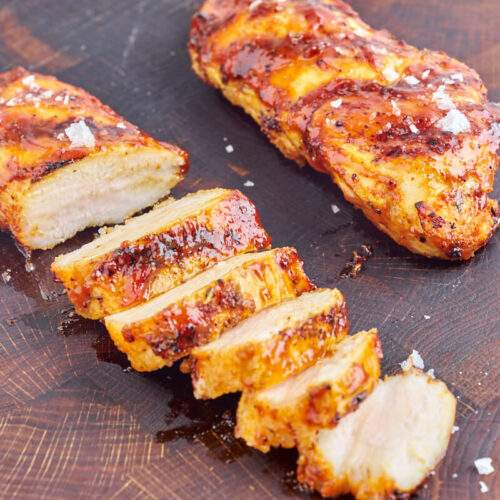 grilled chicken breast slices on chopping board with bbq sauce