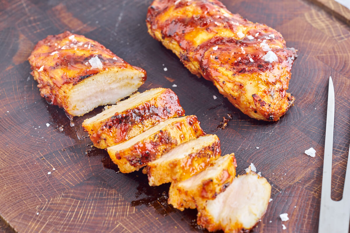 grilled chicken breast slices on chopping board with bbq sauce