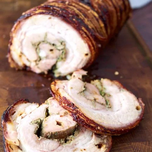 Italian porchetta on wooden cutting board with slices