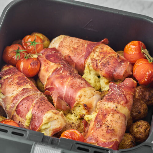 air fryer stuffed chicken breast with ham and cream cheese in air fryer basket with potatoes and tomatoes