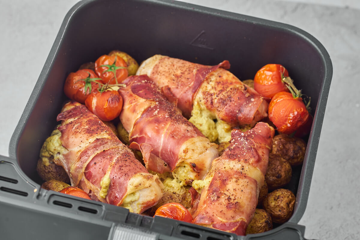 air fryer stuffed chicken breast with ham and cream cheese in air fryer basket with potatoes and tomatoes