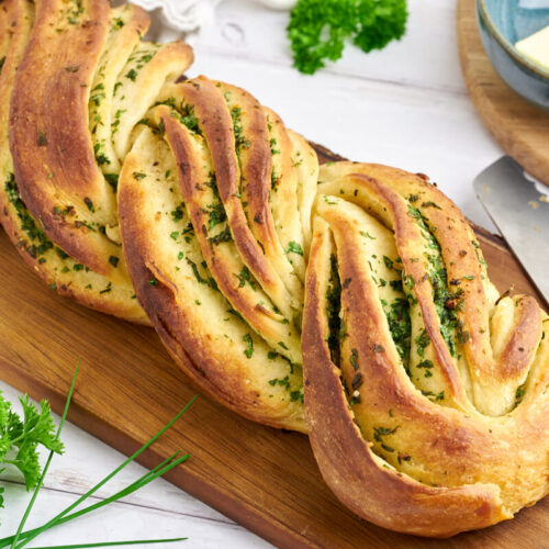 garlic herb bread on a wooden cutting board with a knife