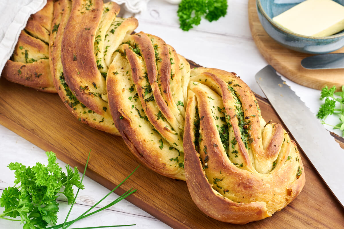 garlic herb bread on a wooden cutting board with a knife