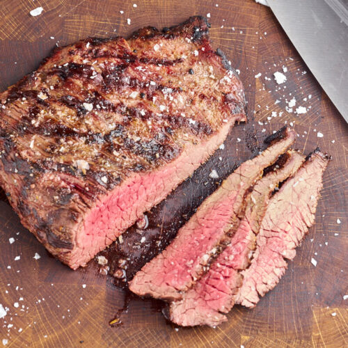 grilled flank steak cut out into thin slices on wooden cutting board