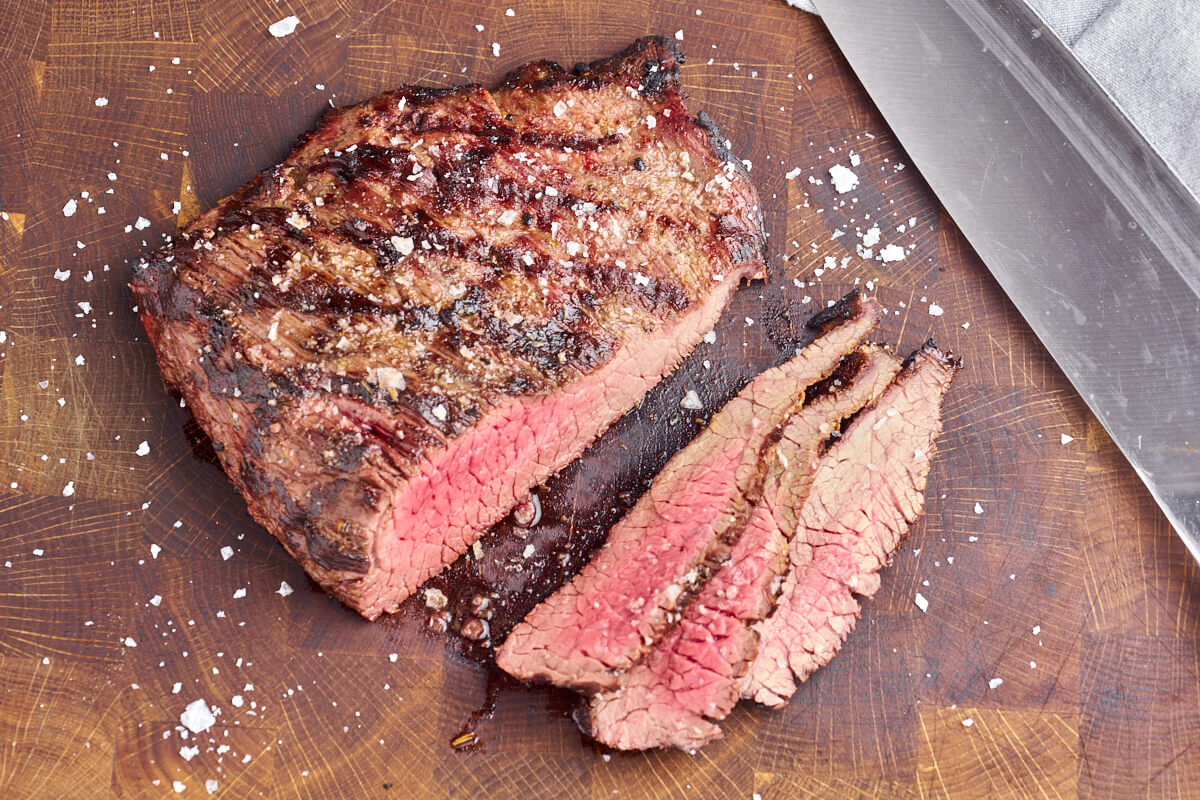 grilled flank steak cut out into thin slices on wooden cutting board