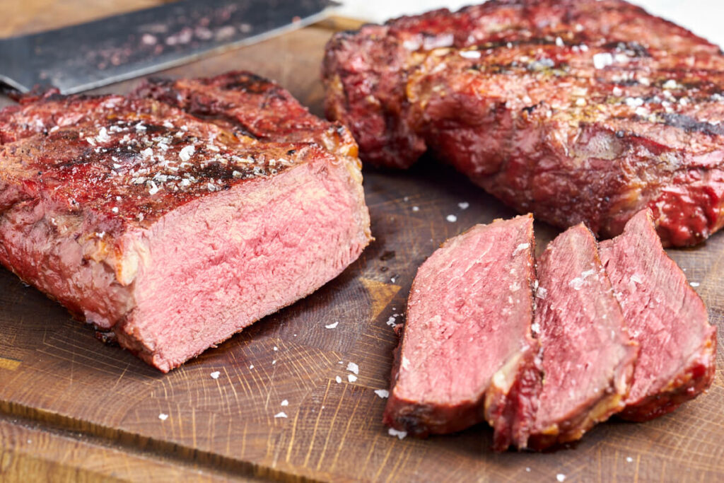 grilled ribeye steak sliced on wooden chopping board