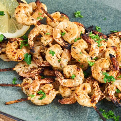 marinated grilled shrimp skewers on plate with lemon slices