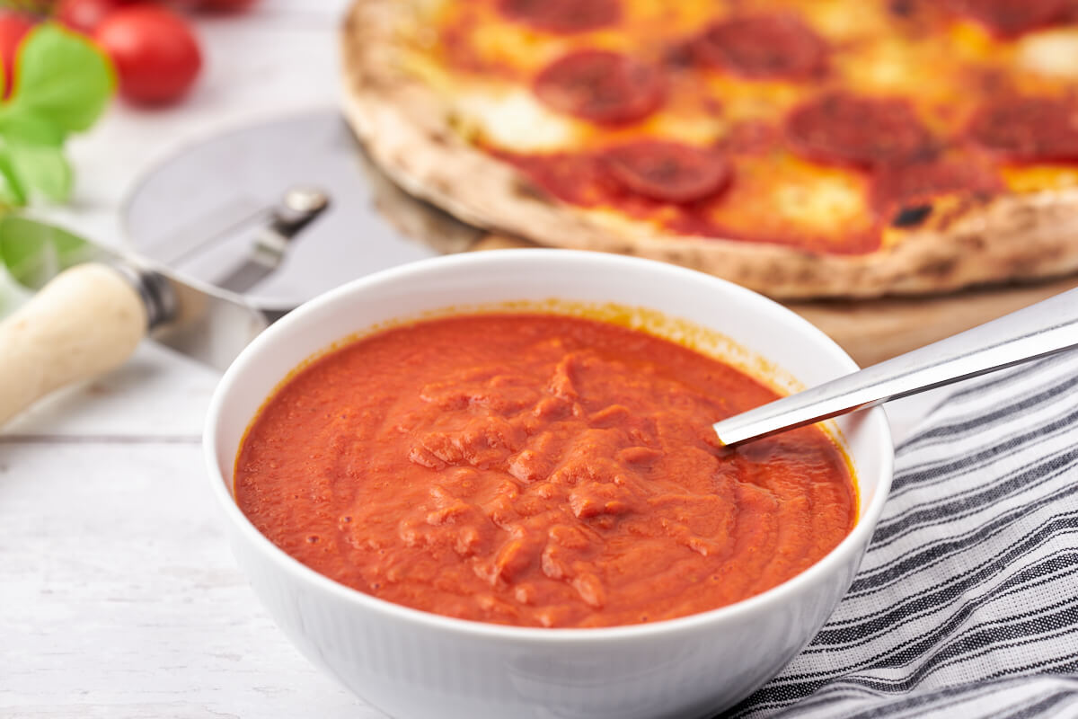 bowl with pizza sauce and homemade pizza behind