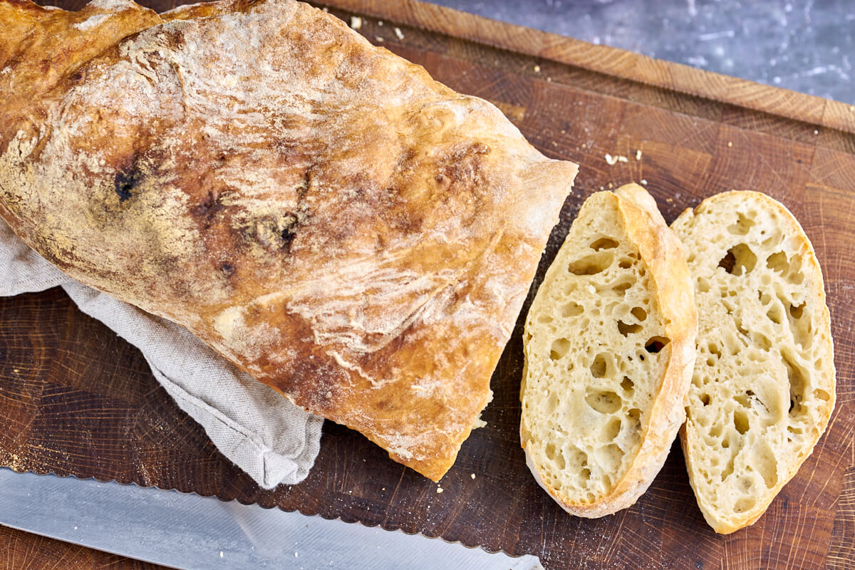 loaf and slices of ciabatta bread on wooden board