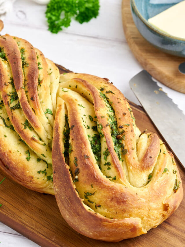 garlic herb bread on a wooden cutting board with a knife