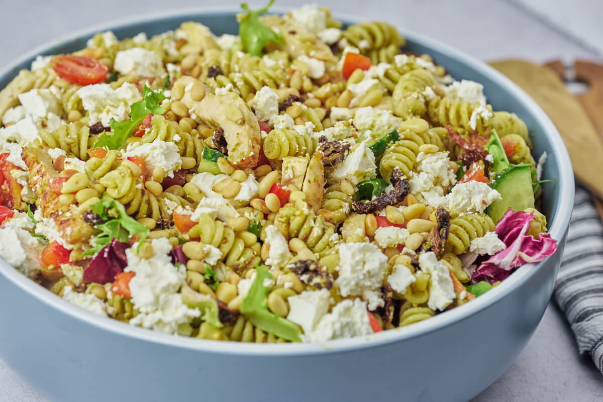 chicken pesto pasta salad with sun-dried tomatoes, feta cheese and pine nuts in bowl