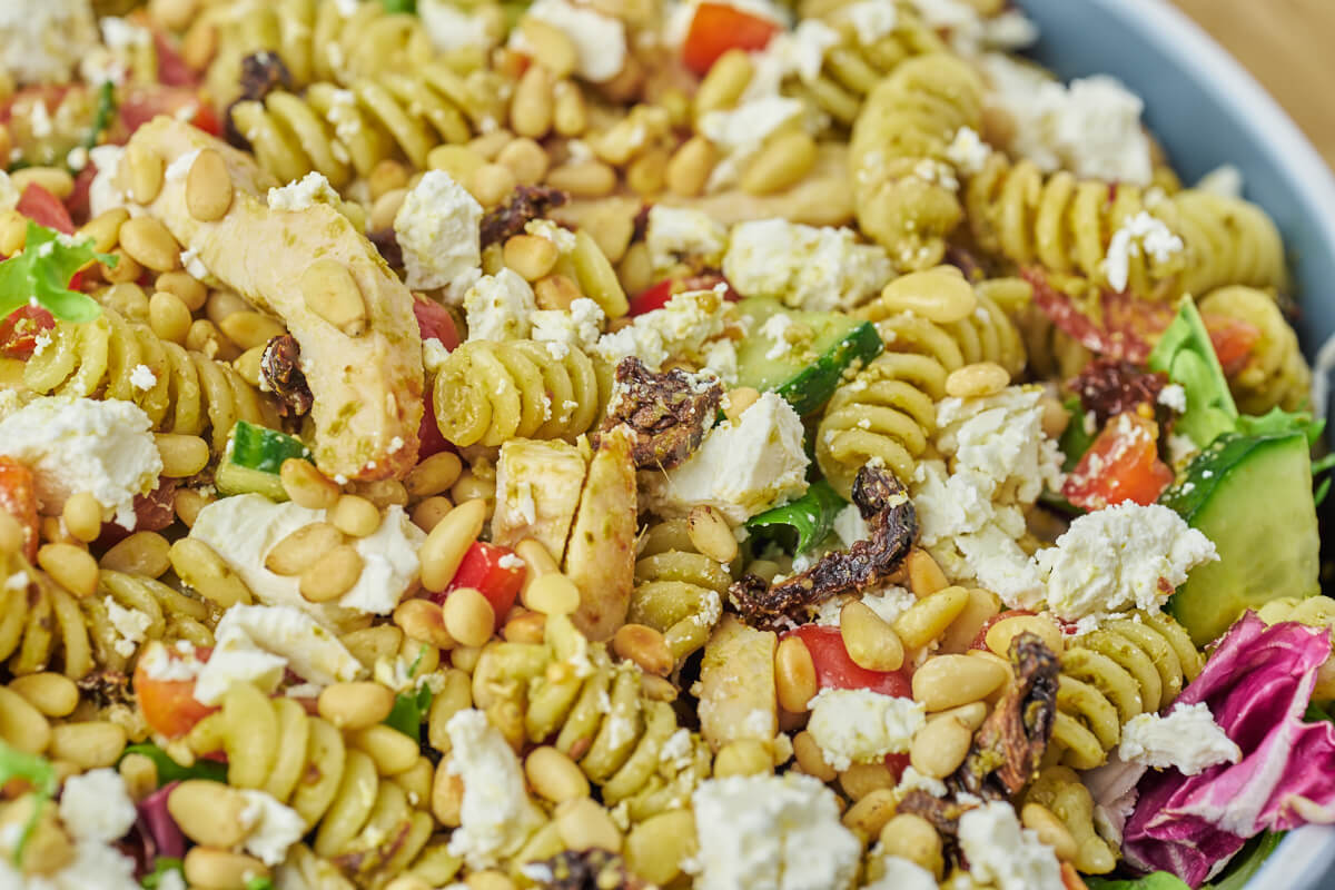 Chicken pesto pasta salad with greens, feta cheese and pine nuts