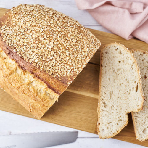 Sliced overnight oat bread on a wooden cutting board with a knife beside it.