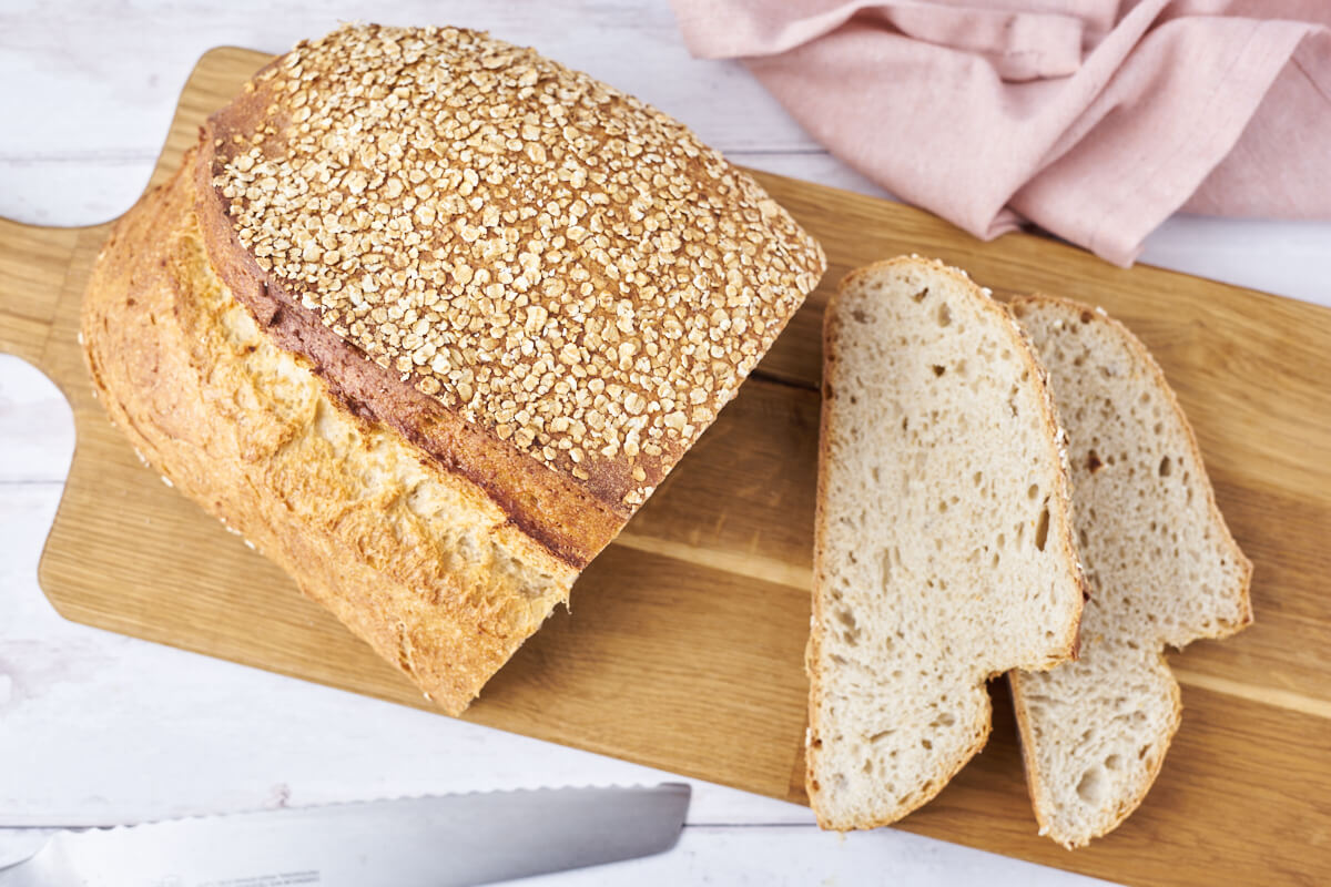 Sliced overnight oat bread on a wooden cutting board with a knife beside it.