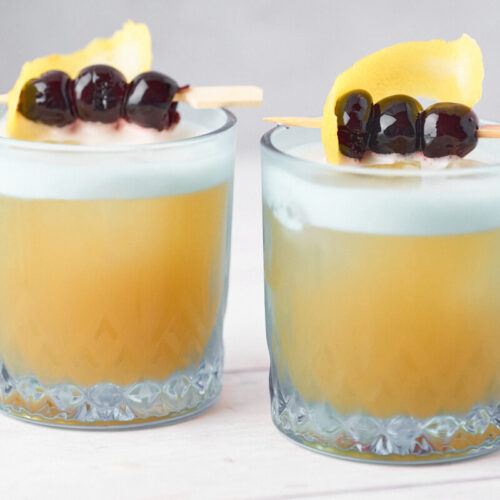 Amaretto sours in two glasses with lemon and cherries as garnish