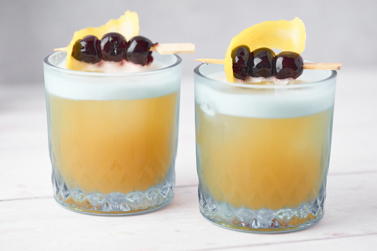 Amaretto sours in two glasses with lemon and cherries as garnish