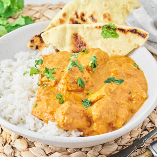 Homemade chicken tikka masala with rice and naan bread, served on a plate with fresh coriander.