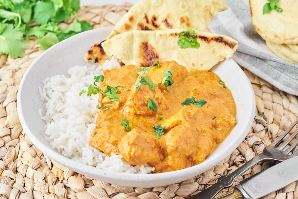 Homemade chicken tikka masala with rice and naan bread, served on a plate with fresh coriander.