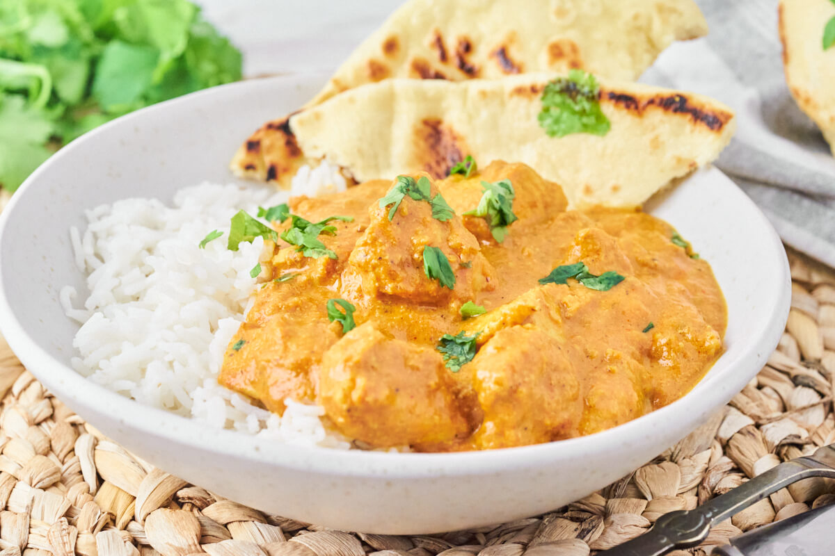 Chicken tikka masala with rice and naan bread, garnished with fresh coriander