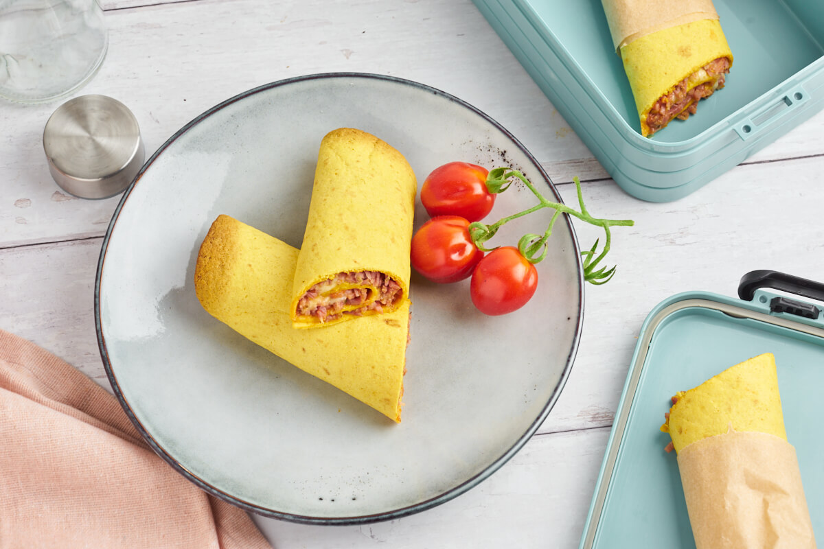 Tortilla rolls with pizza filling on a plate with tomatoes and a lunchbox on the side