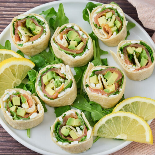 Salmon wraps with cottage cheese and avocado on a plate with salad and lemon