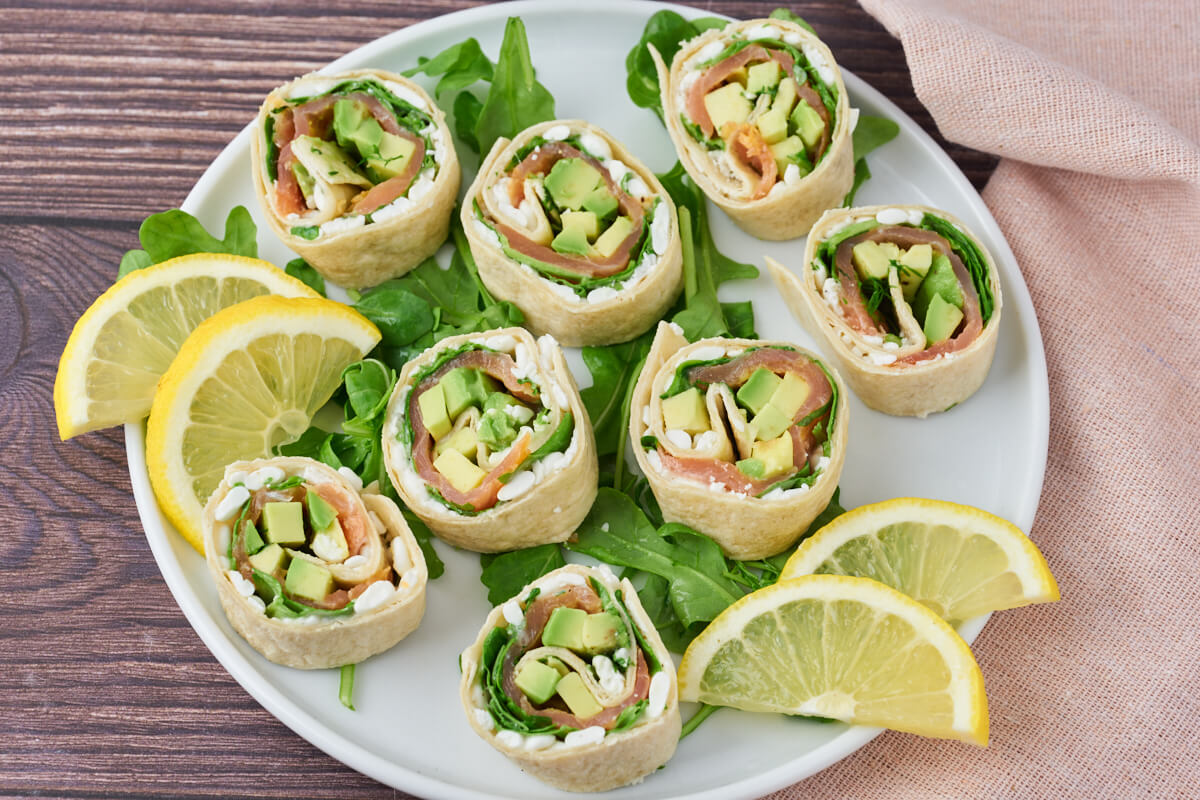 Salmon wraps with cottage cheese and avocado on a plate with salad and lemon