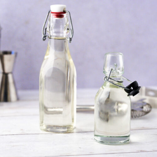 Homemade simple syrup in small bottles with a cocktail shaker in the background