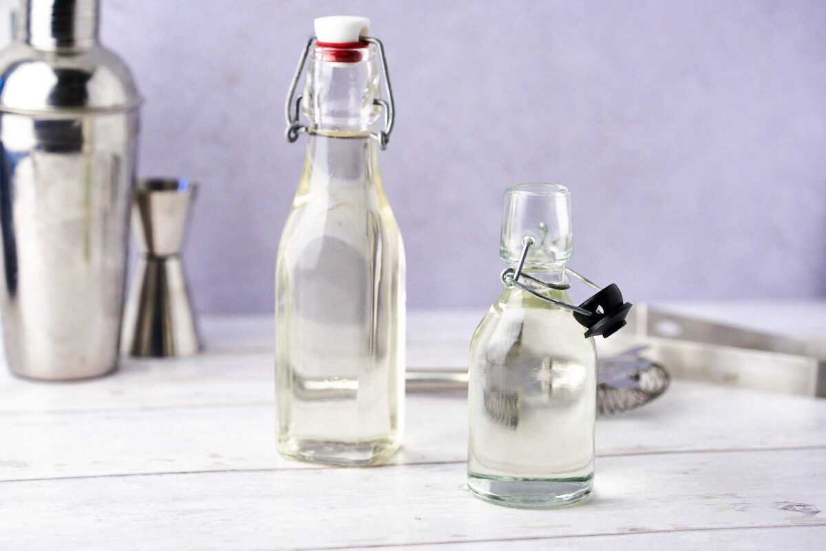 Homemade simple syrup in small bottles with a cocktail shaker in the background