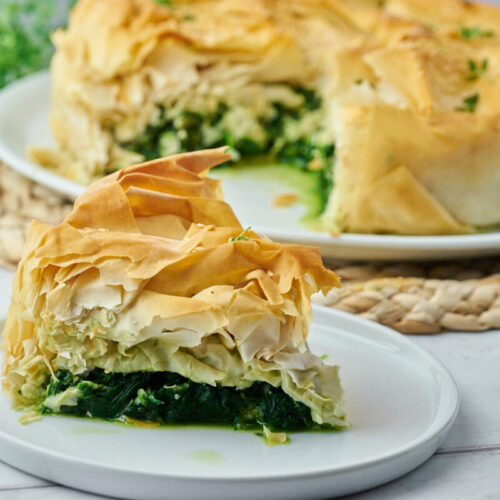 Greek spanakopita with spinach and feta on a plate with a slice of the pie in the foreground