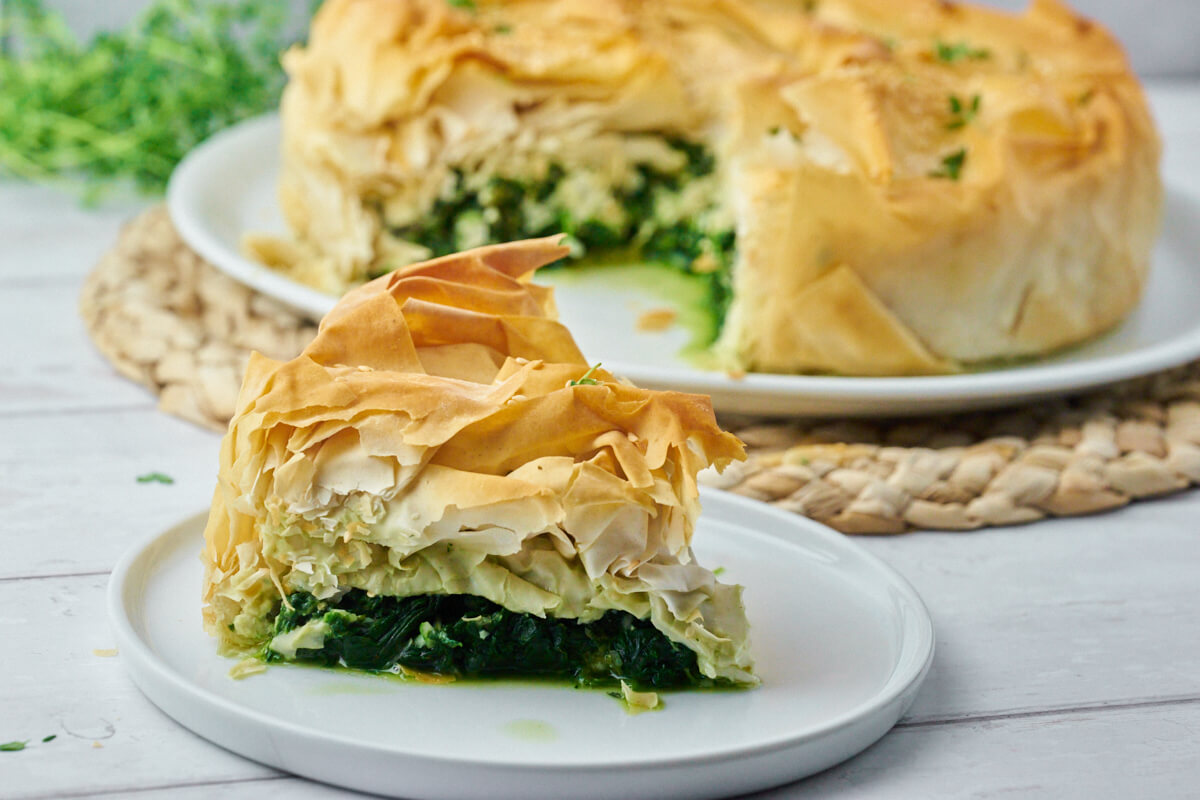 Greek spanakopita with spinach and feta on a plate with a slice of the pie in the foreground