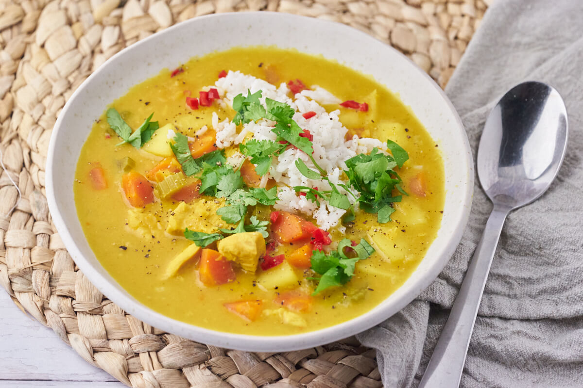 servering of the mulligatawny soup in a bowl with rice, chili and cilantro